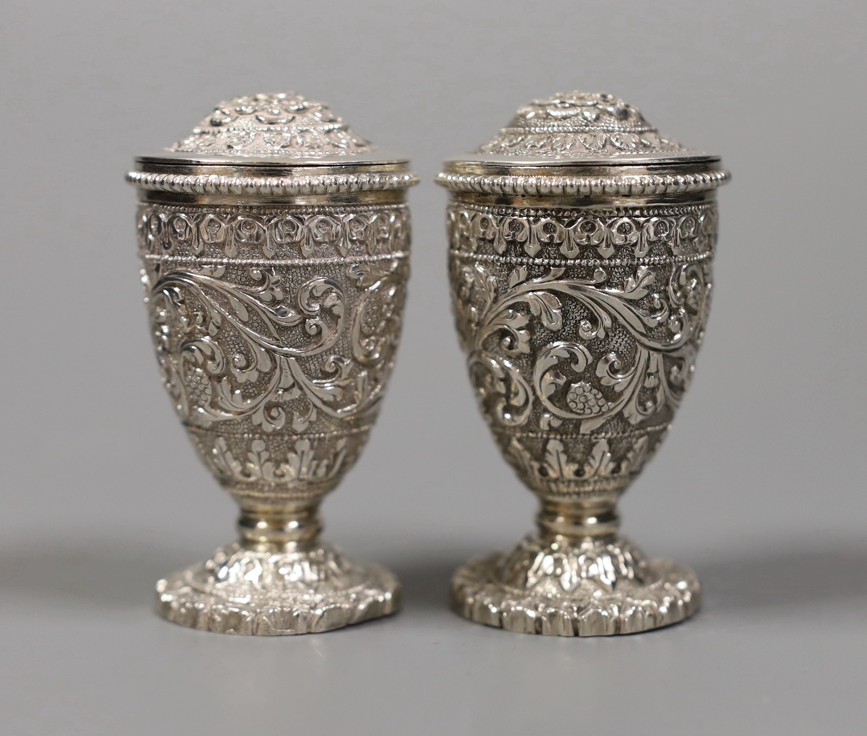 A pair of early 20th century Indian embossed white metal pedestal pepperettes, 7cm, 112 grams, in Elkington & Co, Calcutta, fitted box.